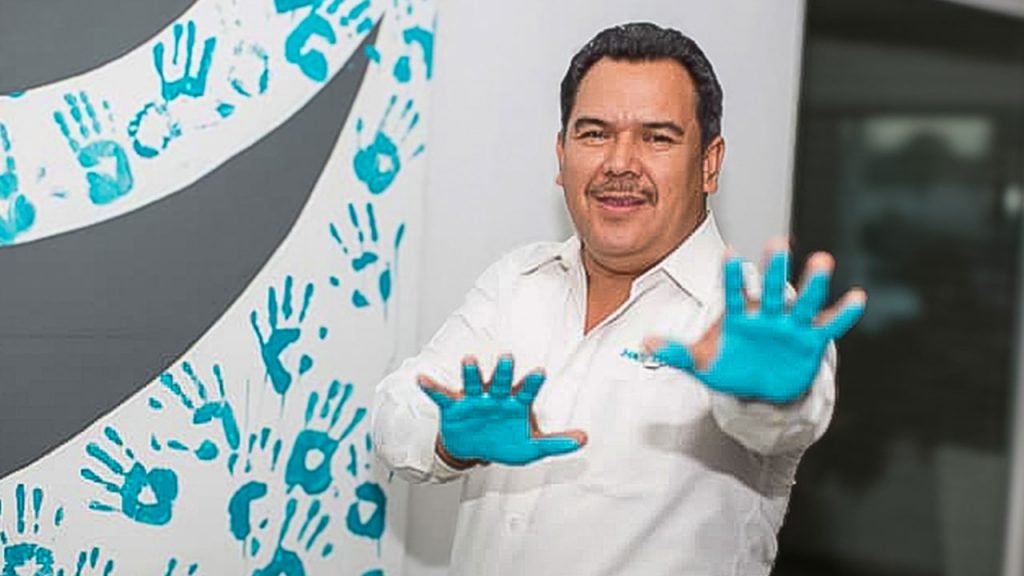 Miembro del equipo de Maqpower sonriendo y mostrando sus palmas de manos pintadas de azul después de ponerlas en un lienzo.